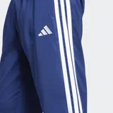 Pantalón Adidas Essentials 3 Rayas de corte clásico, color azul, con cintura elástica con cordón ajustable, bolsillos frontales y puños elásticos. Presenta las emblemáticas tres tiras blancas a los lados de las piernas y el logo de la marca bordado en blanco.