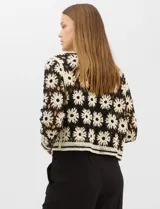 Cardigan abierto de tejido crochet con diseño de flores bicolores en negro y crema. Presenta mangas largas, frente abierto sin cierre y bolsillos frontales tipo parche. Posee terminaciones con franjas a contraste en escote, puños y ruedo.