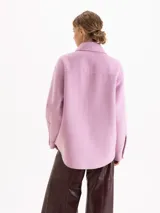 Chaqueta de paño color rosa, con cuello camisero, cierre frontal con botones metálicos y cuatro bolsillos plaqué delanteros. Presenta mangas largas y costuras con pespuntes decorativos al tono.