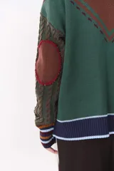 Cardigan de punto con diseño multicolor en tonos marrones, bordó y detalles en amarillo y celeste. Presenta cuello tipo polo, cierre frontal con botones, bolsillos aplicados en el frente y mangas con trama trenzada y coderas bordadas.