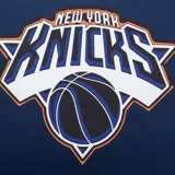 Musculosa de básquet azul marino con detalles laterales en naranja. Presenta el logo oficial de los New York Knicks estampado en el frente y etiqueta de autenticidad NBA en el ruedo.