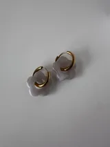 Aros de acero quirúrgico dorado con dije en forma de flor de resina color gris claro.