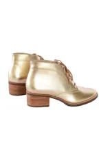 Botín de caña baja con cordones, confeccionado en cuero vacuno metalizado color dorado. Presenta puntera redondeada y tacón bloque texturizado en tono madera.