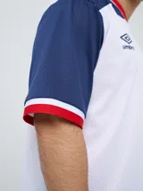 Remera de fútbol Umbro del Club Nacional de Football, de diseño tricolor con cuerpo azul marino, mangas y canesú rojos, y cuello en V con detalles en blanco y azul. Incluye el logo de Umbro en el pecho derecho y el escudo del club en el izquierdo.