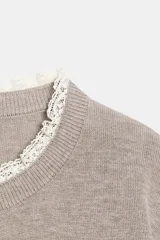 Chaqueta de punto color beige, de manga larga y corte corto, con cuello redondo y puños terminados en puntilla blanca a contraste.