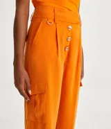 Pantalón cargo de viscosa color naranja, con cintura alta y cierre por enganche doble y botones. Cuenta con bolsillos delanteros, laterales y traseros, y pliegues delanteros.