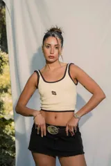 Top ajustado color crema/amarillo claro, con ribetes marrones en cuello y sisas. Presenta un pequeño logo bordado en el centro del pecho.