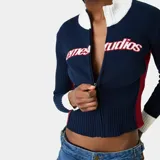Cardigan de punto Eme Studios modelo Betty Navy, de color azul marino con cuello alto y puños blancos, y detalles en rojo en los laterales. Cuenta con cierre frontal de cremallera y logo bordado en relieve en el pecho.