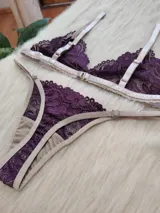 Conjunto de lencería compuesto por un bralette triangular y una bombacha tipo tanga, confeccionados en encaje color violeta con terminaciones y breteles en color tostado.