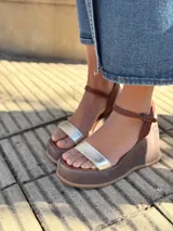 Sandalias de cuero con plataforma, color marrón con tira dorada sobre los dedos y tobillera marrón con hebilla.