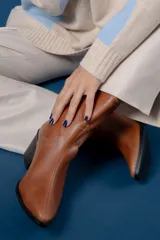 Bota de caña media color chocolate, confeccionada en cuero con textura granulada. Presenta un diseño de estilo western con punta fina, taco cuadrado y una tira lateral decorada con tachas metálicas circulares en tono bronce.