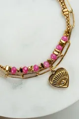 Pulsera dorada de acero quirúrgico con doble cadena, una de eslabones y otra con cuentas rosas. Dije en forma de corazón con ojo grabado y mini cristal.