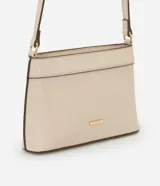 Cartera bandolera pequeña de material sintético color beige con detalles en marrón oscuro. Cuenta con cierre superior por cremallera, asa larga ajustable y placa metálica dorada con el logo de la marca en el frente.
