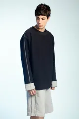 Buzo de felpa negro de corte oversize, con cuello redondo y mangas largas con puños grises doblados hacia afuera. Presenta costuras externas decorativas en tono gris claro a lo largo de las mangas y los hombros.