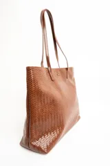 Bolso tipo shopper color marrón de cuero sintético con diseño trenzado. Cuenta con doble asa de hombro y placa metálica con el logo de la marca en el frente.