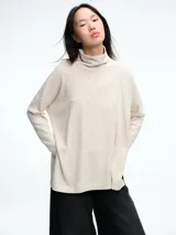 Buzo tejido de silueta holgada en color beige, con cuello alto y mangas largas. Presenta tajos laterales en el ruedo que aportan movimiento a la prenda.