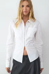 Camisa de popelín blanca con manga larga, cuello clásico, bolsillos frontales con solapa y cierre de cremallera en la parte delantera con abertura en el bajo.