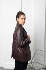 Blazer de eco cuero color bordó, con diseño oversize, hombreras estructuradas y solapas clásicas. Presenta mangas largas con puños vueltos y cierre frontal con botón.
