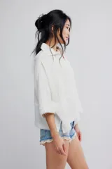 Blusa blanca de algodón vaporoso, con diseño holgado y ligeramente extragrande, cuello camisero, cierre frontal de botones y mangas amplias.