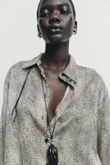 Camisa de manga larga con cuello solapa y cierre frontal de botones. Presenta un estampado de puntos pequeños en tono crema y negro, con puños en contraste que incluyen un estampado más denso.