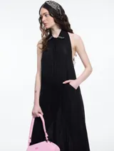 Vestido largo de lino en color azul, con cuello camisero, cierre frontal de botones y espalda descubierta con diseño estilo halter. Presenta un bordado decorativo en el cuello y bolsillos laterales.