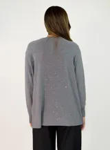 Sweater de punto color beige con sutiles destellos brillantes, cuello redondo, manga larga con puños acanalados y diseño asimétrico con el ruedo trasero más largo que el delantero.