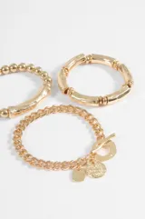 Set de tres pulseras plateadas de diseño variado: una con cuentas cilíndricas, una con cuentas esféricas y una pulsera de cadena con dijes colgantes y cierre de barra.