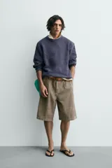 Jersey de hombre de corte relajado, color azul oscuro o morado apagado, con textura rizada (bouclé) y cuello redondo.