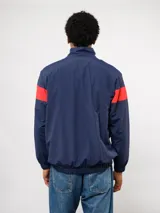 Buzo deportivo de nylon con medio cierre frontal y cuello alto. Presenta un diseño de bloques de color en azul, blanco y bordó, con el escudo del Club Nacional de Football y el logo de Umbro en el pecho.