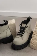 Botas de cuero color beige con suela track negra de goma y cordones gruesos negros. Presentan un diseño de caña baja con costuras visibles y puntera reforzada.