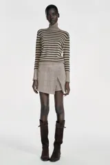 Jersey de punto liso en color beige, con cuello alto y manga larga con detalle de botones metálicos en los puños.