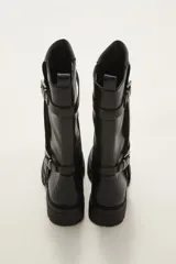 Bota de caña media en color negro, confeccionada en eco cuero con suela track dentada. Presenta un diseño con doble tira ajustable con hebillas metálicas en el lateral externo.