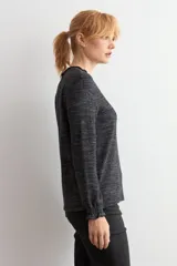 Remera de manga larga con cuello alto tipo media polera, confeccionada en tejido texturado de color beige melange, con puños con detalle de volados.