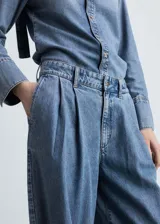 Pantalón de jean estilo wide leg con tiro medio, detalle de pinzas en la cintura, cierre frontal con cremallera y botón, y bolsillos laterales.
