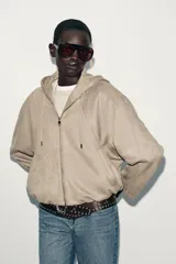 Chaqueta bomber de efecto ante en color marrón, con capucha ajustable mediante cordones, cierre frontal con cremallera, bolsillos laterales y bajo con elástico interior.