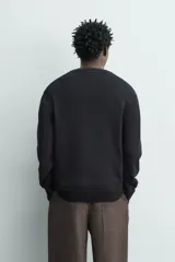 Sweater de punto negro de corte regular fit, confeccionado en algodón con cuello redondo, manga larga y acabados en rib.