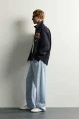 Jeans de denim de algodón en color azul con efecto desgastado, tiro medio y corte recto de ajuste holgado (loose fit). Cuenta con diseño clásico de cinco bolsillos y cierre frontal con cremallera y botón.
