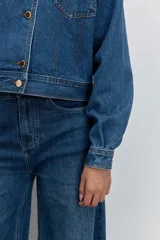 Cazadora de denim azul con corte cropped y diseño de doble botonadura frontal. Presenta un cuello de pana en color bordó y botones metálicos dorados.