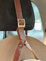 Accesorio porta sombrero de cuero con correa ajustable y hebilla metálica, diseñado para colgarse en el apoyacabezas del automóvil y transportar sombreros de forma segura.