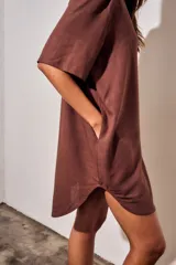 Vestido camisero corto de color marrón, con mangas cortas, cuello camisero, cierre frontal de botones y un bolsillo ojal en el pecho.