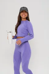 Conjunto deportivo de dos piezas color lila, compuesto por un top de manga larga con diseño seamless y calzas de tiro alto con detalles texturizados en los laterales.