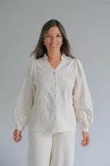 Blusa de color beige con cuello mao y cierre frontal de botones. Presenta mangas largas abullonadas con puños ajustados y un diseño con bordados en relieve de patrones orgánicos en toda la prenda.