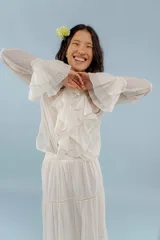 Camisa de estilo romántico confeccionada en algodón, con cuello alto, volados frontales y mangas largas con puños acampanados también decorados con volados.