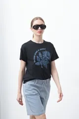 Remera negra de manga corta con estampado botánico en azul y la frase "NOTHING GROWS IN COMFORT".