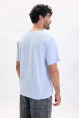 Remera celeste de manga corta, con calce relajado y pequeño estampado tipográfico en el pecho con el texto 'Arrival Coastal Club 1997'.