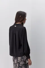 Camisa de manga larga color beige con cuello clásico y botonadura frontal. Presenta mangas con volumen sutil, puños abotonados y una silueta amplia de caída fluida.