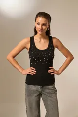 Musculosa negra de bretel fino, con cuello redondo profundo y diseño ajustado al cuerpo. Presenta detalles de studs y strass en la parte frontal.