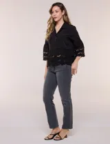 Camisa negra de poliéster con cuello camisero, escote en V y cierre frontal de botones. Cuenta con mangas anchas de corte acampanado y detalles de bordado suizo calado en las mangas y en el ruedo inferior.
