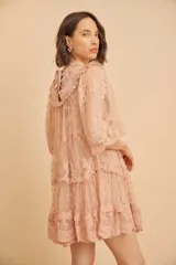 Vestido corto de encaje color durazno, con diseño de volados en capas, mangas largas abullonadas y cuello redondo con detalles bordados.
