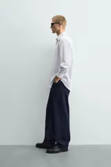 Camisa de corte regular fit confeccionada en tejido de algodón con diseño de rayas verticales finas. Presenta cuello italiano, manga larga con puños abotonados y cierre frontal mediante botonadura.